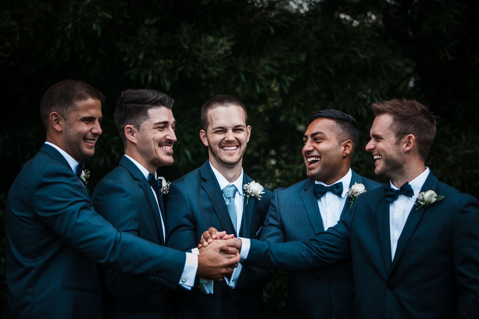 Five groomsmen in navy suits laughing together