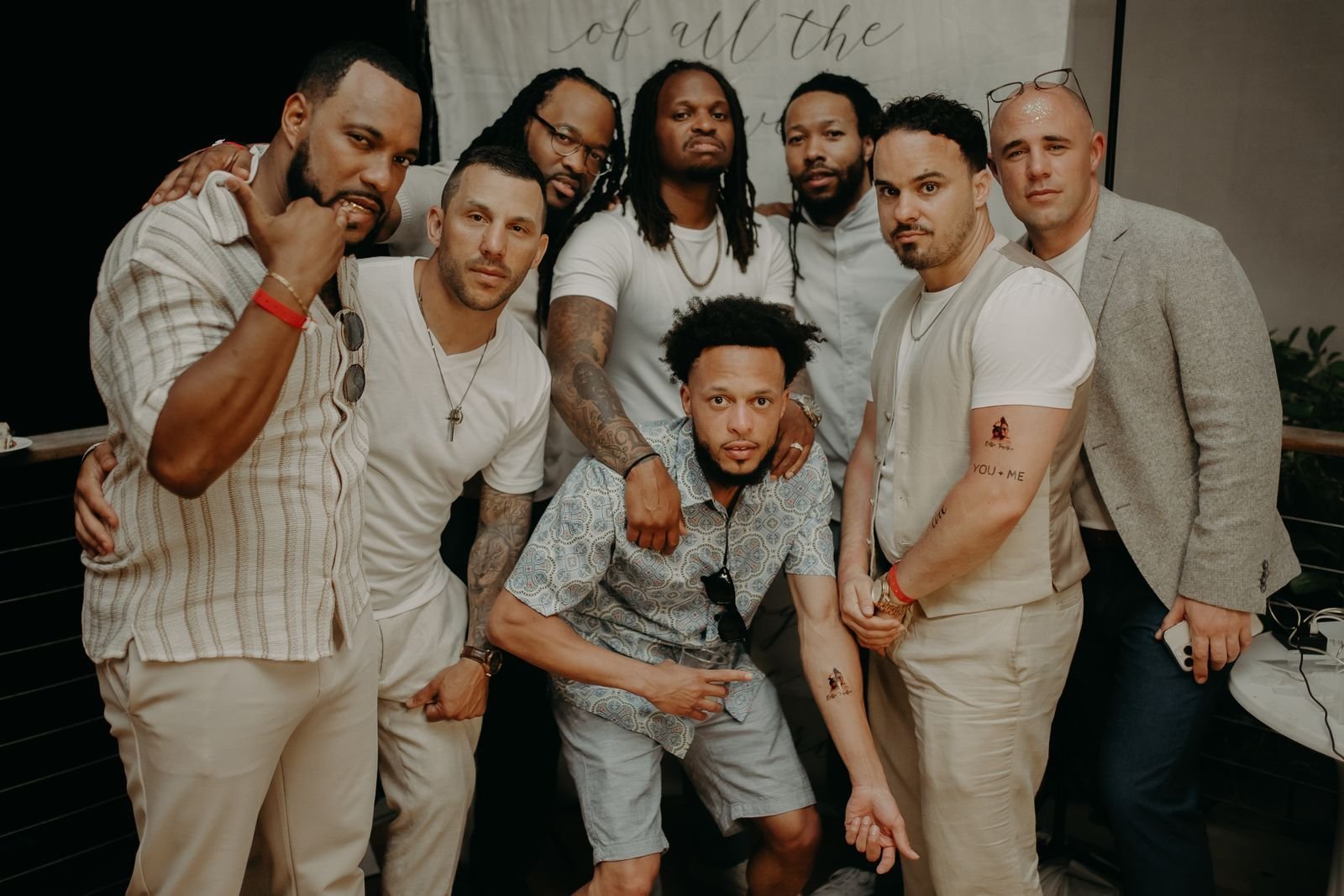 Eight guys in white and cream posing together at a party